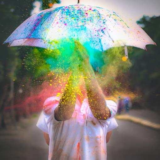 Boy sheltering from multicoloured powder under umbrella.