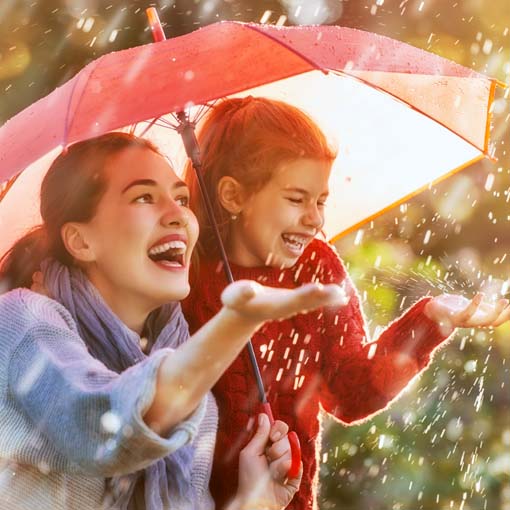 Mother and daughter under umbrella during rain shower.