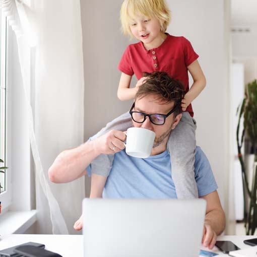 Child sitting on father's shoulders while father works